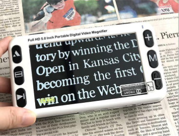 Elektronická přenosná lupa položená na novinách, která daný text zobrazuje zvětšený a s invertovanými barvami